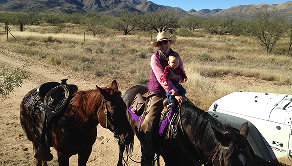 Una dona ranxera de l'estat d'Arizona, amb el seu fill petit en braços, participa en les tasques de gestió de bestiar. Autora: Sarah King